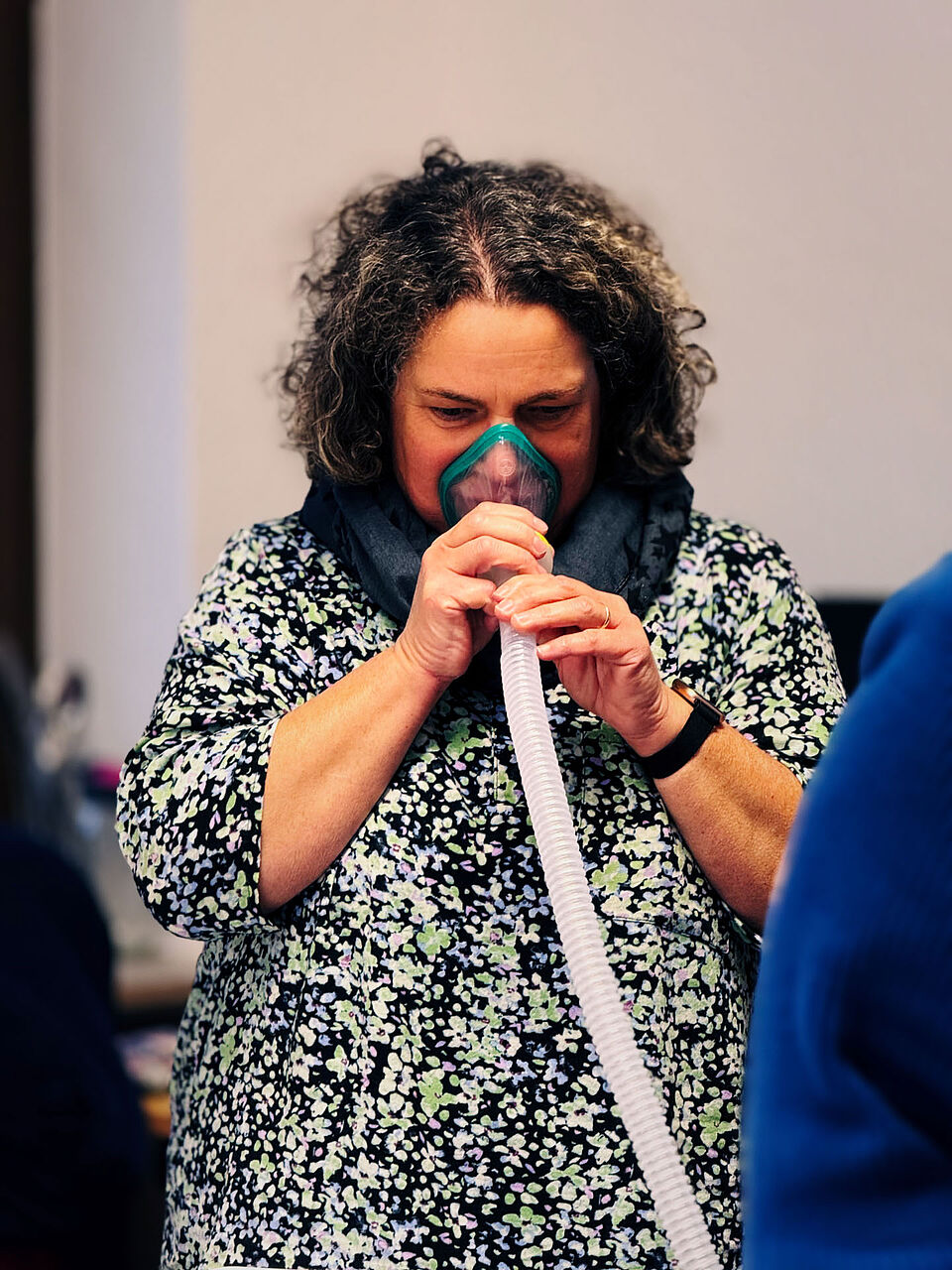 Krankenpflegekraft probiert Hustenassistent mit Schlauch in der Hand und Maske auf Gesicht