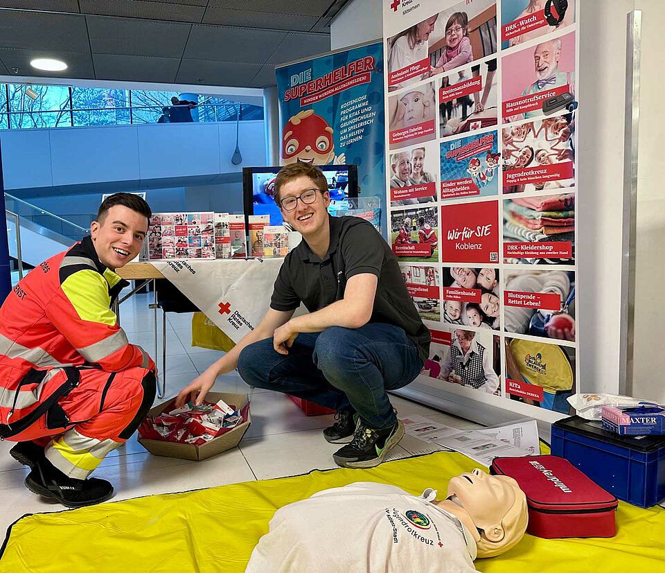 Rettungsdienstmitarbeiter vor Logowand und Reanimation-Trainingspuppe