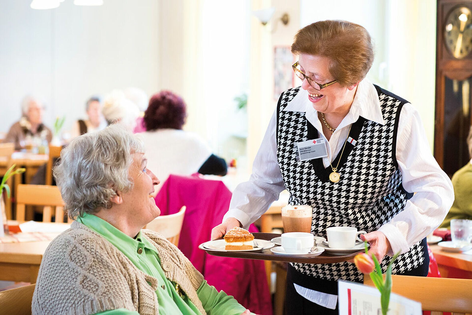 Seniorin serviert anderer Dame Kaffee und Kuchen auf einem Tablett