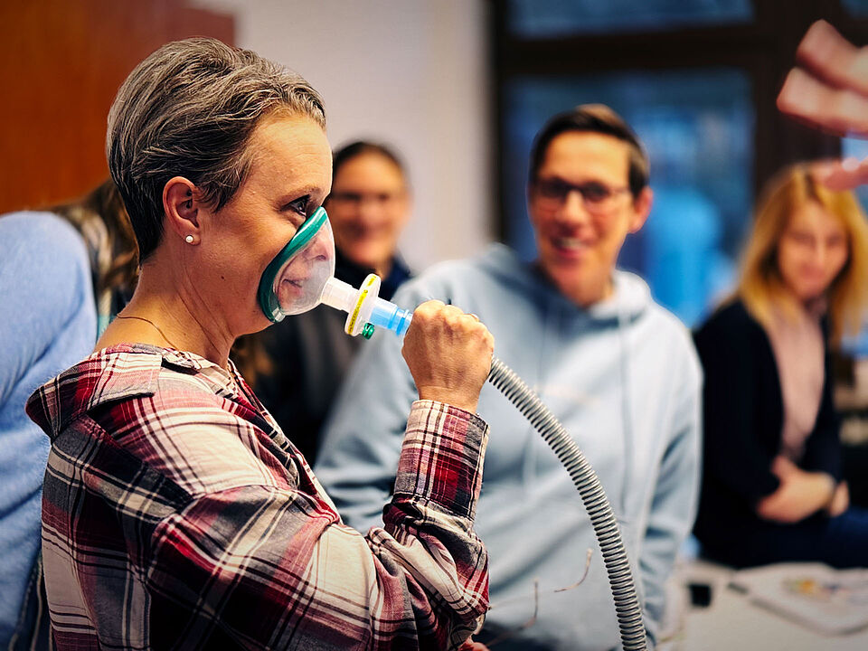 Krankenpflegekraft probiert Hustenassistent mit Schlauch in der Hand und Maske auf Gesicht
